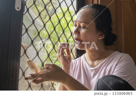 Woman is sitting in a room and applying makeup 133806965
