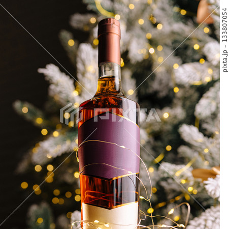 Holiday spirit with whiskey bottle wrapped in lights near Christmas tree 133807054