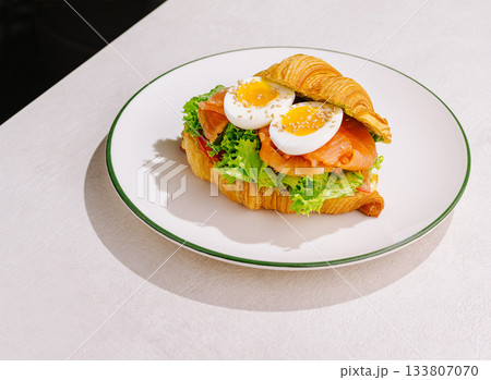 Tasty croissant sandwich with smoked salmon and eggs on a plate 133807070