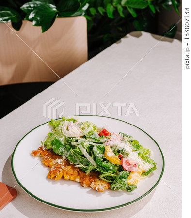 Fresh salad and grilled fish served on a white plate in a restaurant setting 133807138