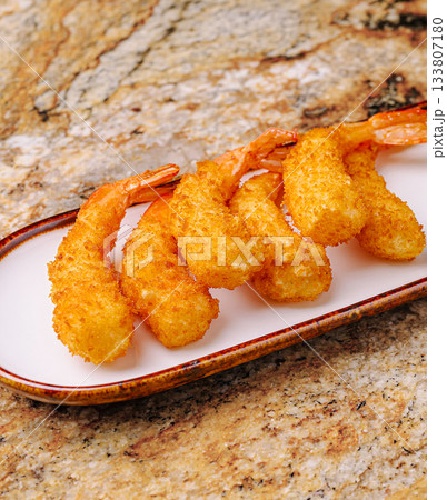 Golden fried shrimp served on a white plate with a textured background 133807180