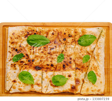 Freshly baked flatbread garnished with spinach on a wooden board 133807239