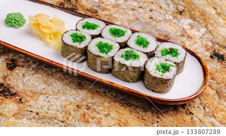Delicious sushi rolls displayed on a plate with green wasabi and ginger 133807289