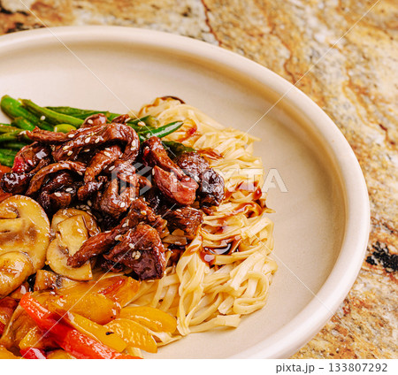 Delicious stir-fried beef with vegetables and noodles on a plate Delicious stir-fried beef with vegetables and noodles on a plate 133807292