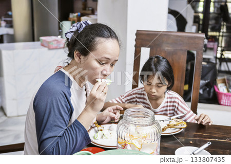 Indonesian woman and a child are having meal in dining table. They are enjoying the food while eating together 133807435
