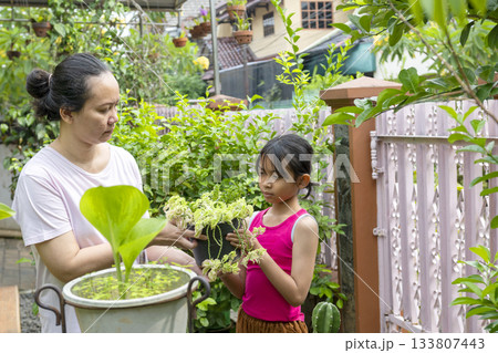 Woman and a girl are holding plants in a pot 133807443