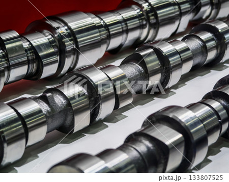 Close view of multiple shiny camshafts displayed against a bright background emphasizing their detailed craftsmanship and mechanical design Close view of multiple shiny camshafts displayed against a bright background emphasizing their detailed craftsmanship and mechanical design 133807525
