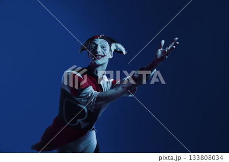 Jester reaching forward on dark blue stage with engaging theatrical expression 133808034