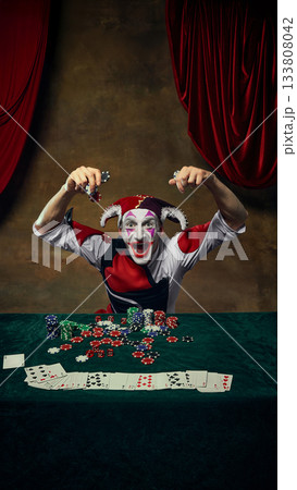 Joker lifting poker chips in both hands over table Joker lifting poker chips in both hands over table 133808042