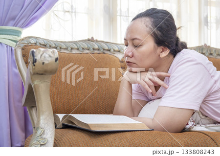 Woman is laying on a couch with a book in her lap Woman is laying on a couch with a book in her lap 133808243