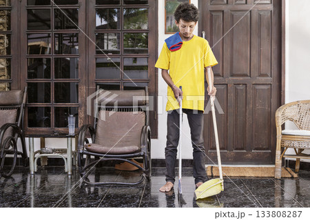 Young man in a yellow shirt is cleaning the floor with a broom. Cleaning concept 133808287