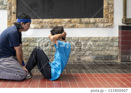 Asian man is helping a boy do sit ups 133808407