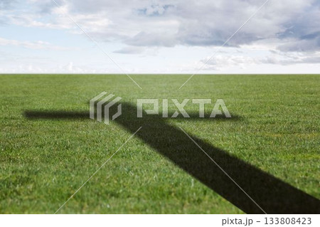 Shadow of cross-shaped structure is casting across grass field under cloudy sky, in flat design Shadow of cross-shaped structure is casting across grass field under cloudy sky, in flat design 133808423