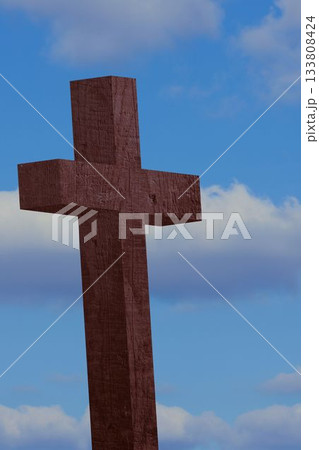 Wooden cross is standing against blue sky showing wood grain and scattered clouds in flat design Wooden cross is standing against blue sky showing wood grain and scattered clouds in flat design 133808424