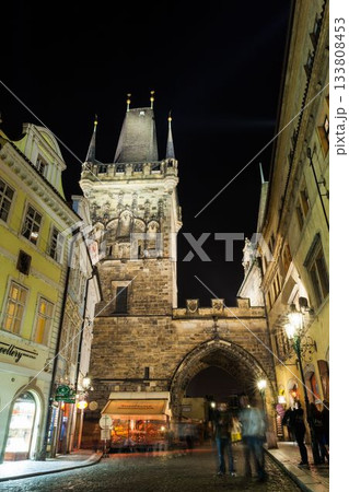 Showing 2D flat medieval gateway arch rising above cobbled road casting lamp glow on moving figures 133808453