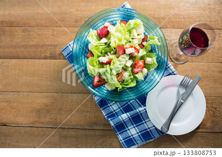 Fresh salad in bowl with red wine on wooden table 133808753