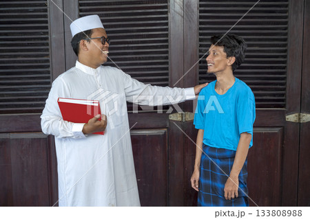 Muslim man in a white robe is talking to a young man in a blue shirt 133808988