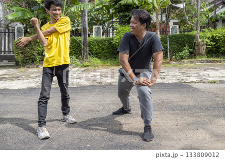 Two Indonesian southeast asian men talking while doing warm up before exercise outdoors. Sport activity Two Indonesian southeast asian men talking while doing warm up before exercise outdoors. Sport activity 133809012