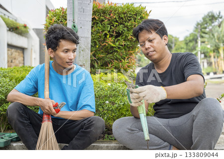 Two Indonesian southeast asian gardeners men sitting and resting while talking after doing some gardening in the backyard. Gardening work 133809044
