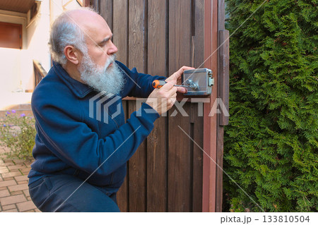 Senior man adjusting fence lock with concentrated precision during home repair Senior man adjusting fence lock with concentrated precision during home repair 133810504