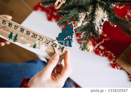 Close-up of hands adjusting wooden advent calendar shaped like a Christmas tree next to festive decorations. Advent calendar trends, countdown to Christmas, holiday anticipation, seasonal traditions Close-up of hands adjusting wooden advent calendar shaped like a Christmas tree next to festive decorations. Advent calendar trends, countdown to Christmas, holiday anticipation, seasonal traditions 133810567