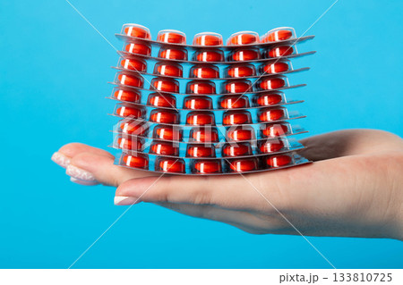 Stack of pills on the palm of the hand on a blue background, close-up. Concept of vitamins in pharmaceuticals, close-up 133810725