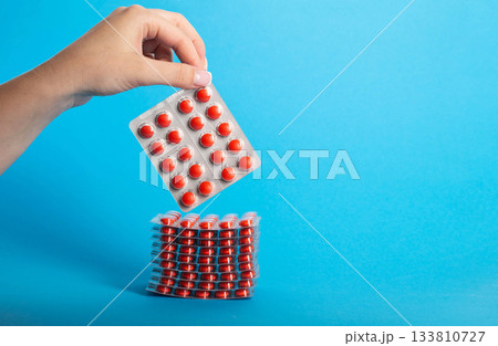 Female hand holding a blister pack with red pills on a blue background. Concept of lozenges for cough and sore throat, close-up. Copy space for text, treatment 133810727