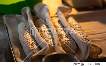 Unbaked bread dough baguettes covered with cloth, rising on baking sheet, preparation of homemade bakery goods, uncooked raw loaves ready for oven, kitchen cooking process 133810806