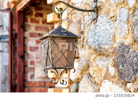 A forged retro lamp hangs on a stone wall, close-up, architecture A forged retro lamp hangs on a stone wall, close-up, architecture 133810824