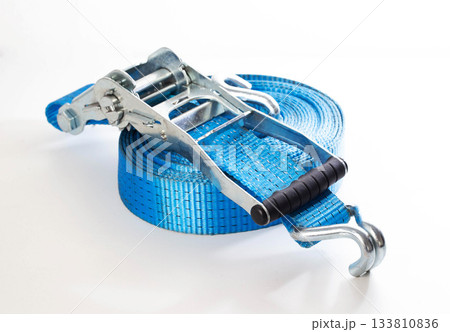 Blue ratchet strap coiled on white background. Heavy duty cargo tie down equipment with metal hooks and tensioner. Safety and securing load tool 133810836