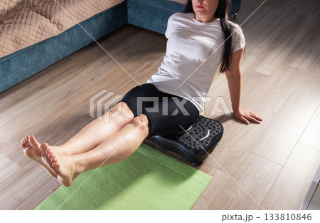 Brunette girl exercises at home on a vibration platform for weight loss. Home exercise machine for sports. Copy space for text, healthy Brunette girl exercises at home on a vibration platform for weight loss. Home exercise machine for sports. Copy space for text, healthy 133810846