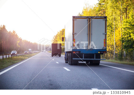 A refrigerated truck transports perishable food cargo along a highway in summer against a sunset backdrop, industry. Copy space for text 133810945