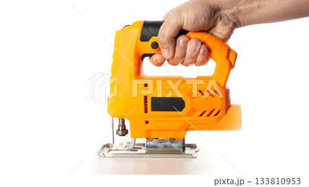 A yellow electric jigsaw in a worker's hand against a white background, isolated, close-up. Woodworking tool, industry 133810953
