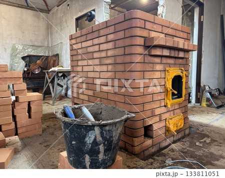 Construction of a heating stove. The ash pan and stove door are wrapped with tape. The stove shelf is visible. Stove fitters tools and materials are nearby. 133811051