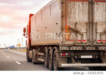 Commercial semi truck trailer driving highway road during sunset or sunrise sky; heavy goods vehicle with dirty rear doors and taillights; cargo transport industry logistics 133811075