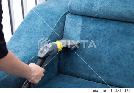 Cleaning a blue sofa with a vacuum cleaner in a bright living room during daylight hours 133811321