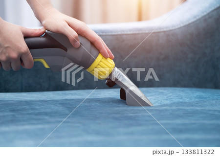 Cleaning upholstery with a handheld steam cleaner in a bright living room setting during the day Cleaning upholstery with a handheld steam cleaner in a bright living room setting during the day 133811322