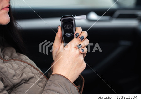 Woman In Automobile Examines Alcohol Tester Reading. Hands Holding Digital Sobriety Check Tool. Woman In Automobile Examines Alcohol Tester Reading. Hands Holding Digital Sobriety Check Tool. 133811334