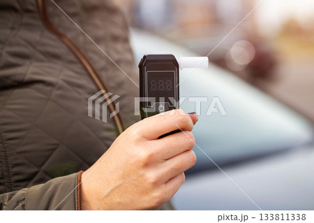 Female Hand Holds Portable Alcometer With Display. Checking Sobriety Next To Automobile. Copy space for text 133811338