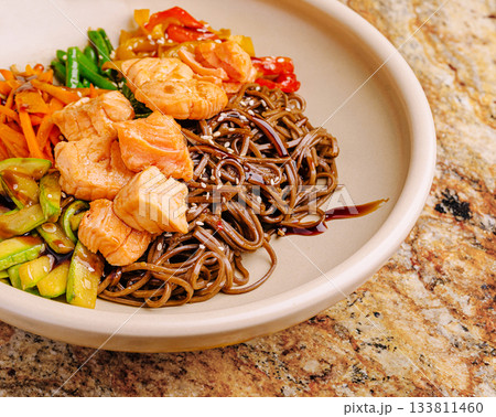 Salmon and soba noodle bowl with colorful vegetables on a textured surface 133811460