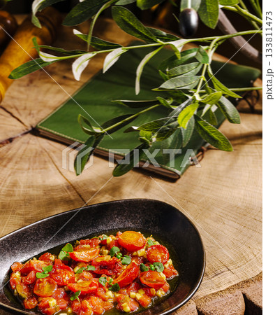 Fresh tomato dish served on a black plate with greens in a rustic setting 133811473