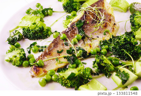 Freshly cooked fish with broccoli, peas, and herbs on a white plate 133811548