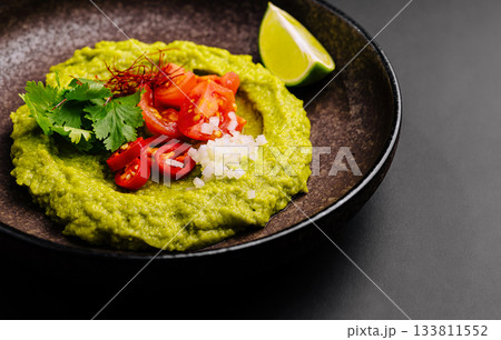 Delicious green avocado dip served with fresh toppings and lime wedge Delicious green avocado dip served with fresh toppings and lime wedge 133811552