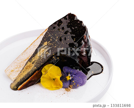Dark chocolate cake slice with decorative flowers on white plate 133811698