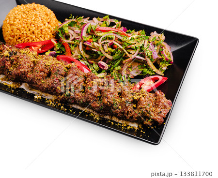Delicious grilled kebab served with rice and fresh salad on a black plate Delicious grilled kebab served with rice and fresh salad on a black plate 133811700