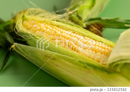 fresh corn cob with husk on green background 133812582