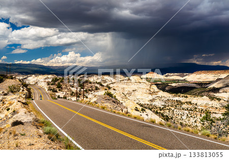 Utah State Route 12 winds over The Hogback in Grand Staircase-Escalante National Monument, United States. A large, dramatic storm cloud with rain, virga, hangs over the vast slickrock landscape 133813055
