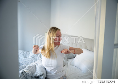 woman stretching happily in bright cozy bedroom 133813224