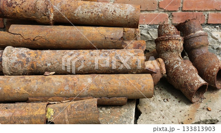 Rusty water pipes lying on the ground near a brick wall, used corroded iron, replacement of drainage pipes, dismantling old rotten pipes covered with a layer of rust, oxidation of metal water pipes Rusty water pipes lying on the ground near a brick wall, used corroded iron, replacement of drainage pipes, dismantling old rotten pipes covered with a layer of rust, oxidation of metal water pipes 133813903