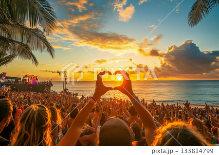People gather on the beach during a lively festival as the sun sets, creating a beautiful backdrop for celebration and joy 133814799